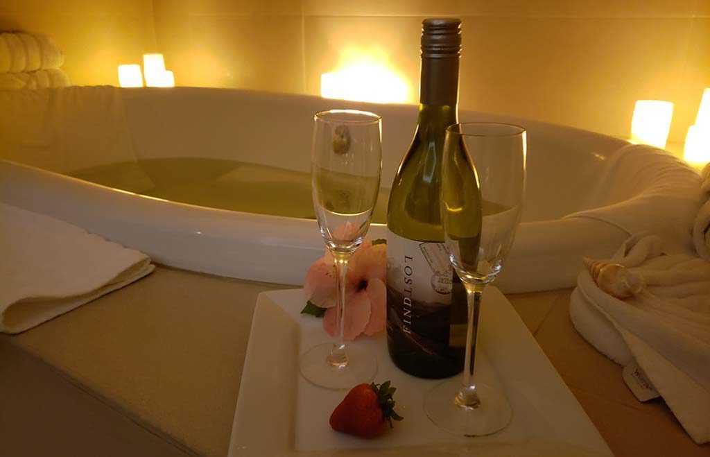 a bottle of wine and two glasses sit by a full bathtub surrounded by glowing candles